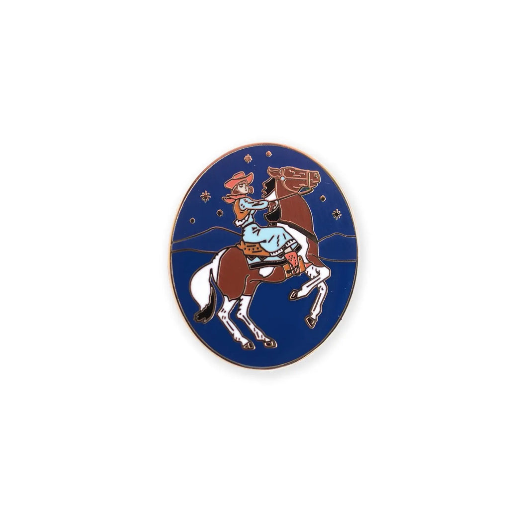 Royal blue hat pin with a cowgirl riding on a brown horse in a night sky with a drawing of simple mountains and stars. 