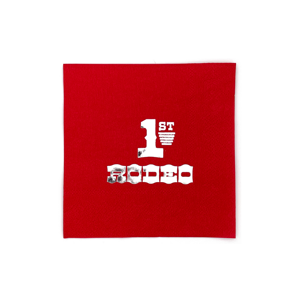 Red, square cocktail napkin with silver foil text that says "1st Rodeo"